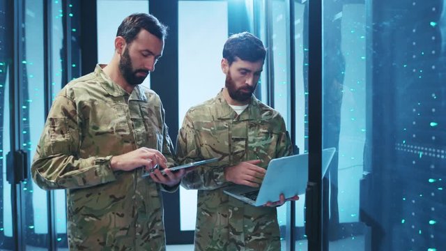 Two military experts in uniform inspecting modern cyber security, using laptop and digital tablet, web hosting and intercepting secret information. Data center.
