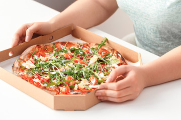 Fastfood. Chubby girl sitting at kitchen table with pizza box close-up
