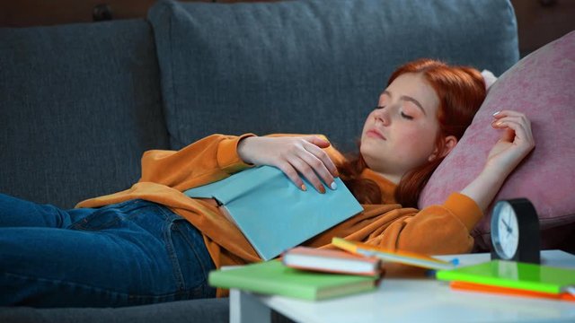 tired teenage girl, awakened by alarm clock, lying on sofa