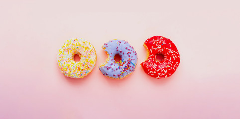 Bitten colored donuts with colorful sprinkles on pink background. Copy space