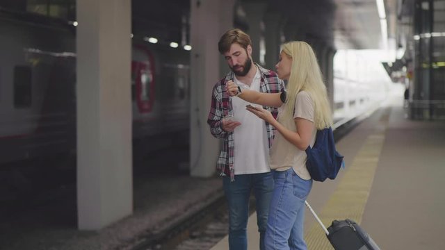 Young couple standing on train platform waiting for delayed train