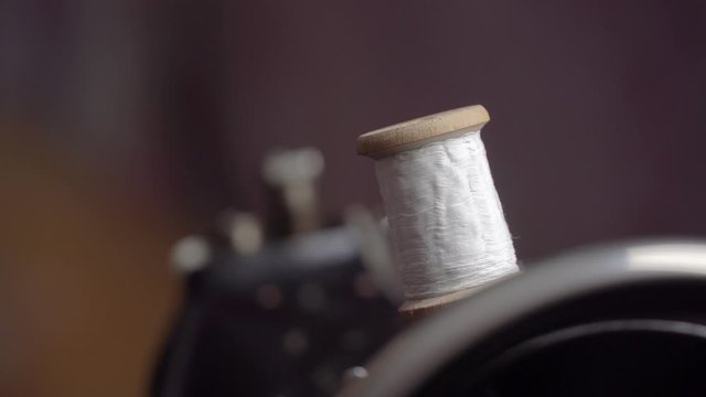 Thread is Wound on a Robbin. Close-up of a Spool with Thin Thread on Working a Vintage Sewing Machine. Spool with thin white thread on working a sewing machine. Sewing bobbin being wound up on a