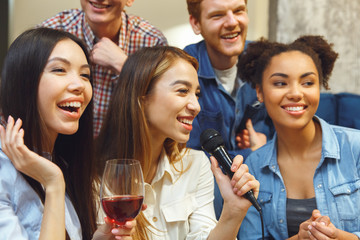Group of friends having party indoors fun together girl holding microphone close-up
