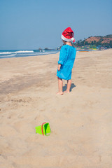 Baby girl in santa hat on a sandy beach.