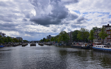 Amsterdam, Holland, August 2019. View of the river on the Amstel river, outskirts of the city. Big boats moored on a sunny day with blue sky and white clouds.