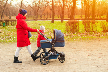 Happy mother walking with baby stroller in park. Happy parenting and healthy lifestyle concept. Woman with baby stroller walk