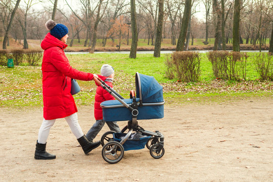 Happy mother walking with baby stroller in park. Happy parenting and healthy lifestyle concept. Woman with baby stroller walk