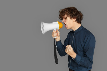 Copy Space for Text or Product. Teenager boy standing isolated on grey shouting loud at megaphone