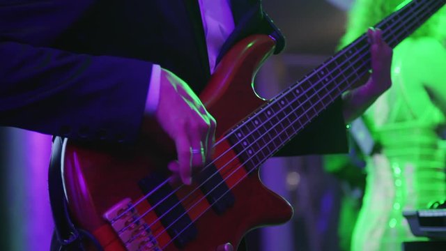 Musician with guitar and band perform at wedding celebration in banquet hall. American man and woman stars playing, singing on dark stage for guests of festive event. Concept: music, people, lifestyle
