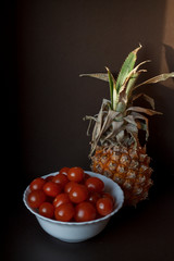 healthy food: ripe pineapple and cherry tomatoes on a dark background