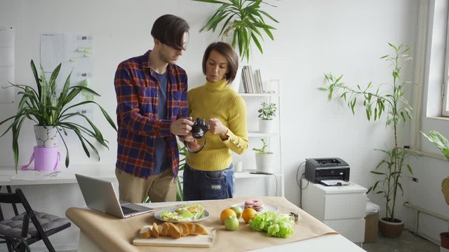 Female flatlay stylist helping male photographer to take food background pictures with fruits and meals placed on table in office
