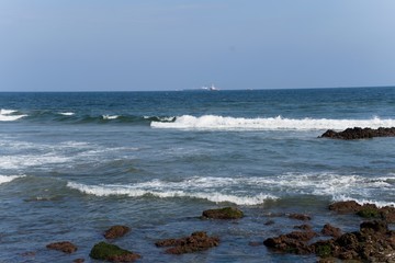 Sea with tidal waves and stone under blue sky.