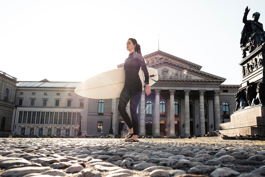 Young woman with surfboard on the way to Eisbach, Munich, Germany