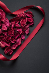 Red petals and silk ribbon shaped in the shape of a heart on a black background, congratulations concept