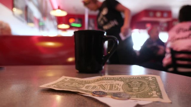 Tips, check and cup of coffee on the table of American diner. Waiters serve tables on background.