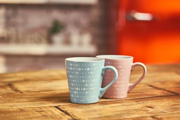 Two cups on wooden table, kitchen with red fridge in the background.
