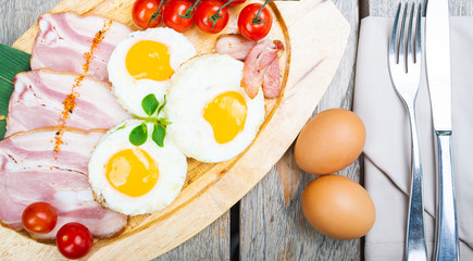 Tasty fried eggs with vegetables on a wooden plate.