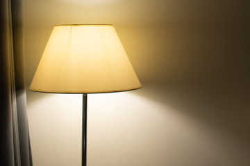 A yellow floor lamp against a white wall in a dimly lit room.