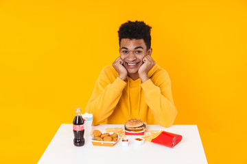 Happy african teenager boy eating fast food meal