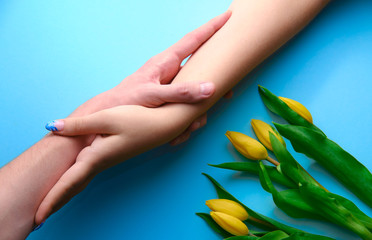 Holding hands on blue background with tulips, topdown view, holidays concept