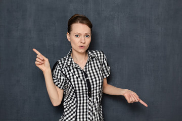 Portrait of unhappy puzzled young woman pointing in opposite sides