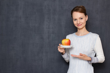 Portrait of happy young woman pointing at plate with ripe apple