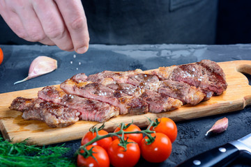 Marbled beef steak. The man is salting the medium-rare meat. Freshly made chuck roll steak.