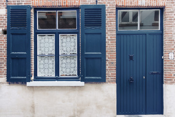 Fototapeta na wymiar Old house exterior with blue painted door and window shutters. Classic blue 2020 year color trend concept