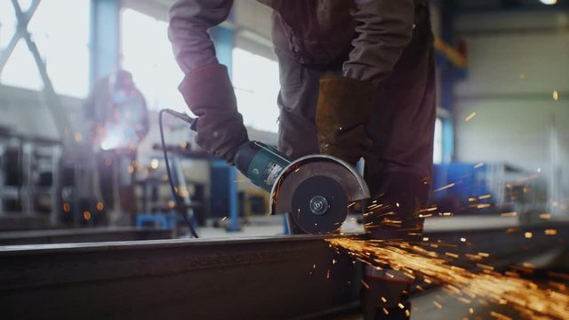man in working wear cuts beam at construction site closeup