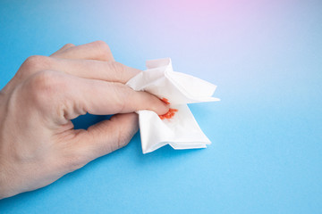 Cut finger holds a napkin. Blood on the hygiene napkin. Skincare mockup for design on a blue background. Cosmetology concept. Bloody wound