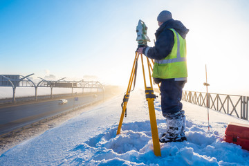 Surveyor near the bridge. Geodesy. Total station Man with a tachometer. Work on the observation of the deformation of the bridge. Topographic and geodetic work. Russia. Saint Petersburg. Winter.
