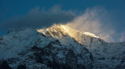 Sunlight falls on the icy ridge around the cloud-covered peak of Annapurna South in the Nepal Himalaya.