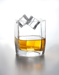 Studio isolated splashing whiskey over white background. Two ice cubes fall into a glass of whiskey