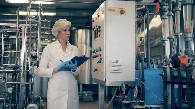 Female engineer, factory worker checks machines at a modern plant, factory. Female worker controls the quality of production equipment.