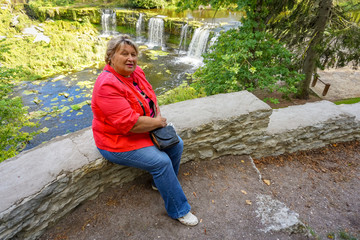 Mature plump woman in red resting at the waterfall