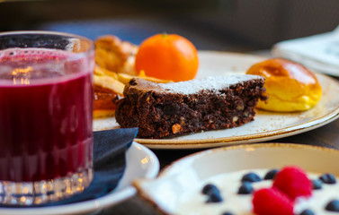 breakfast table detail with chocolate cakes, jam, red orange juice, mandarin, yogurt with raspberries and blueberries - 309275293