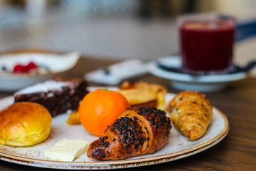 detail of breakfast table with chocolate cakes, jam, red orange juice, mandarin, croissants, butter, yogurt with raspberries and blueberries - 309275296