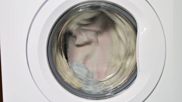 Washing machine door with rotating garments inside. focus in the center of dirty laundry and washing machine on the frame
