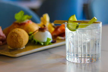 gin tonic with lemon and a tray of typical Napolitan snacks such as buffalo mozzarella, savory puff pastry, black pig salami from Caserta, ham and cheese - 309275429