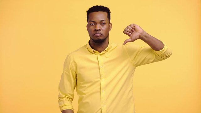 displeased african american man showing thumb down isolated on yellow