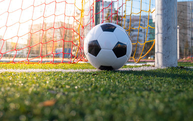 Shot from the ground. The ball on the soccer goal line. Green grass, white line, colorful net from the football gate, shadows, bright sun.