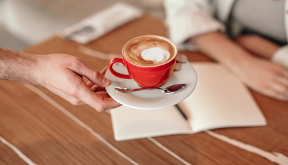 Crop waiter giving coffee to client