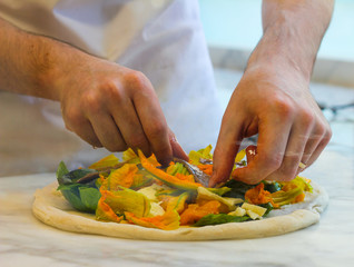 pizza maker prepares a pizza with zucchini flowers, fresh mozzarella, cetara anchovies and yellow tomatoes of Vesuvius