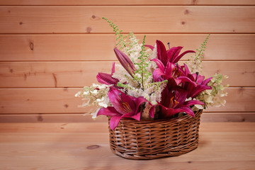 Wicker basket with purple lilies and white astilbe and hydrangea flowers on wooden table. Selective focus. View with copy space.