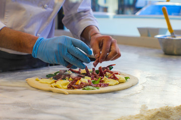 pizza maker is preparing a Spicy gourmet pizza with yellow Piennolo tomatoes, Caserta salami, chilli pepper strands, Agerola provola and parmesan cheese in an Italian pizzeria - 309278607