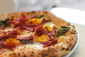 close detail of Spicy gourmet pizza with yellow Piennolo tomatoes, Caserta salami, chilli pepper strands, Agerola provola and parmesan cheese in an Italian pizzeria