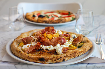pizzeria table set with pizza with corbarino yellow tomato, black Casertano pork ham, chopped pistachio and buffalo stracciatella