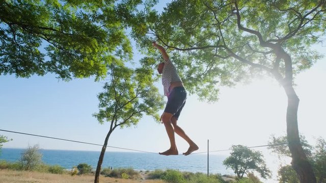 Athlete walking in slackline in the park with sea and blue sky on background	