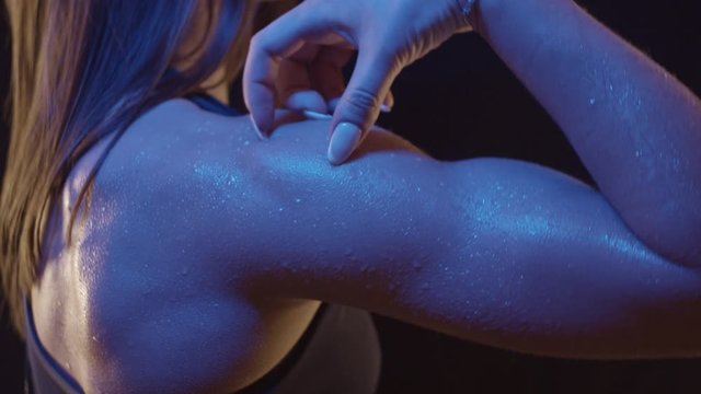 Arm muscles of fit woman under colored light with drops of water, close up, shot in slow motion