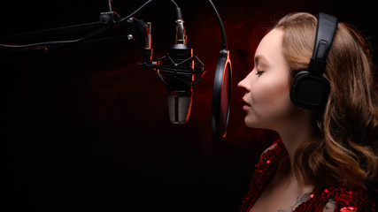 Vocalist, celebrity sings in a studio microphone with headphones on her head, live performance,...